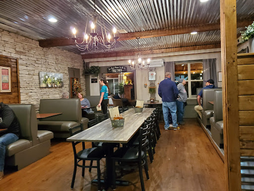 Guests seated in the dining room at The BBQ Place Porch & Grill, with wood booths, a chandelier and a corrugated metal ceiling