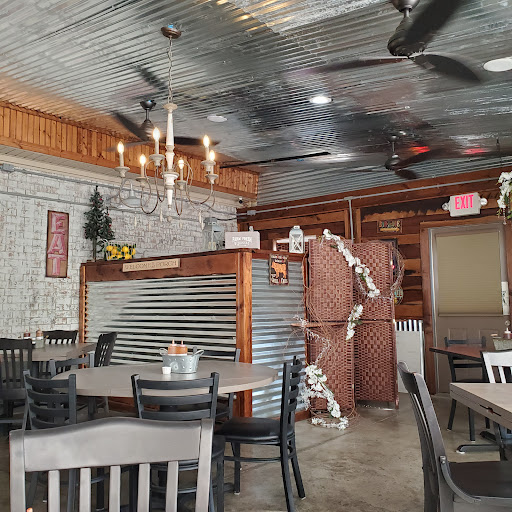The interior of The BBQ Place with a corrugated metal ceiling, ceiling fans and a large EAT sign on the brick wall