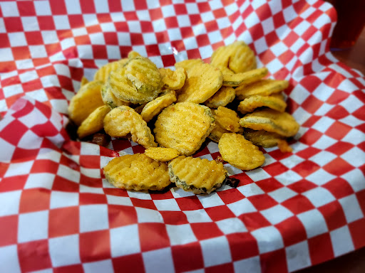 A basket of golden fried pickles served on red-and-white checkered paper at The BBQ Place Porch & Grill